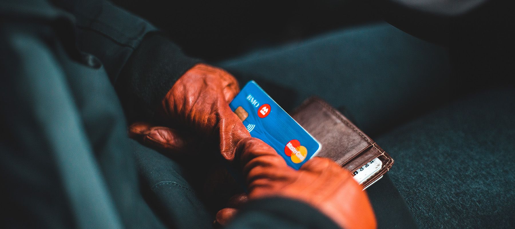 BMO Cashback Mastercard held snuggly with hands wearing 2 red leather gloves on top of a wallet